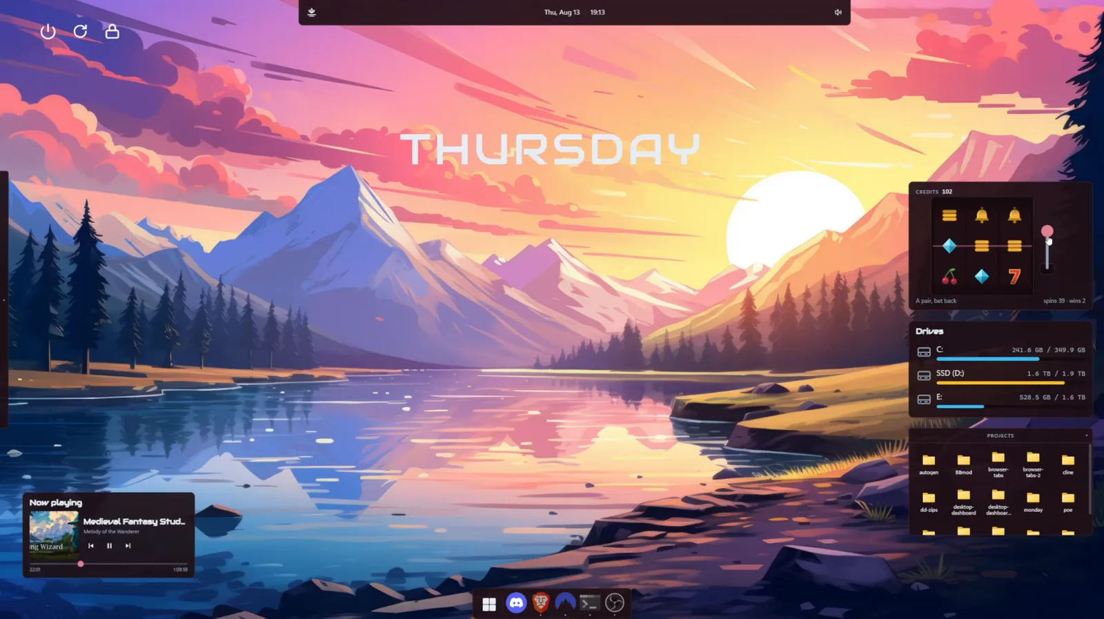 A desktop over a sunset mountain wallpaper, with the day name across the sky, a slot machine widget, drive meters, a projects drawer and a now playing card.